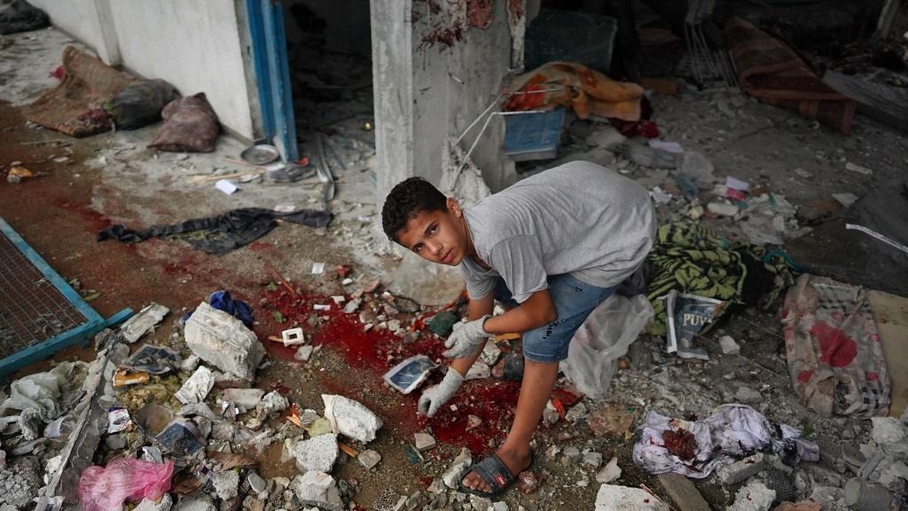 Egy palesztin fiú ellenőrzi a törmeléket egy vértócsa körül a Gázai övezet középső részén fekvő Nuseiratban, az izraeli bombázás során eltalált, kitelepített embereket befogadó ENSZ-iskolánál.