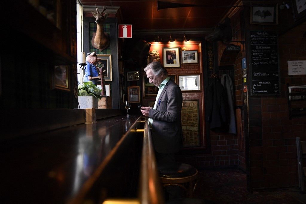 A man checks his phone drinking a glass at the 'Half Way In' pub in central Stockholm, Sweden on March 23. 2020. Bars and restaurants in Sweden are still open despite the corona virus outbreak, even if you can notice much less guests at the restaurants. (Photo by ALI LORESTANI / TT News Agency / AFP) / Sweden OUT