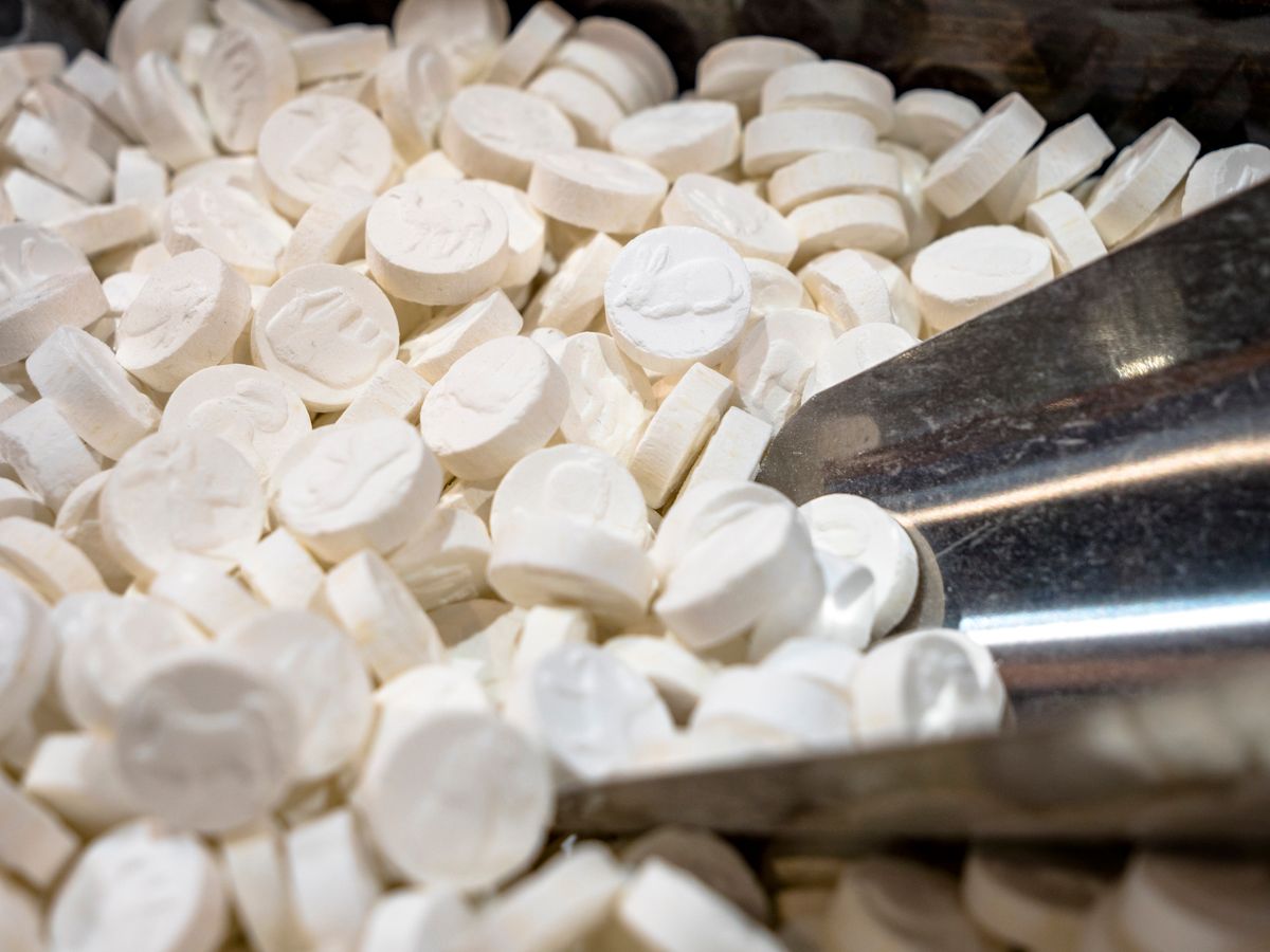 Large Selection of white pills resembling perscription medication, mints and illegal drugs such as MDMA, Yabba and Acid  pictured with a serving measuring scoop. Concept piece for social issues, illicit drugs, organised crime and addiction, extasy