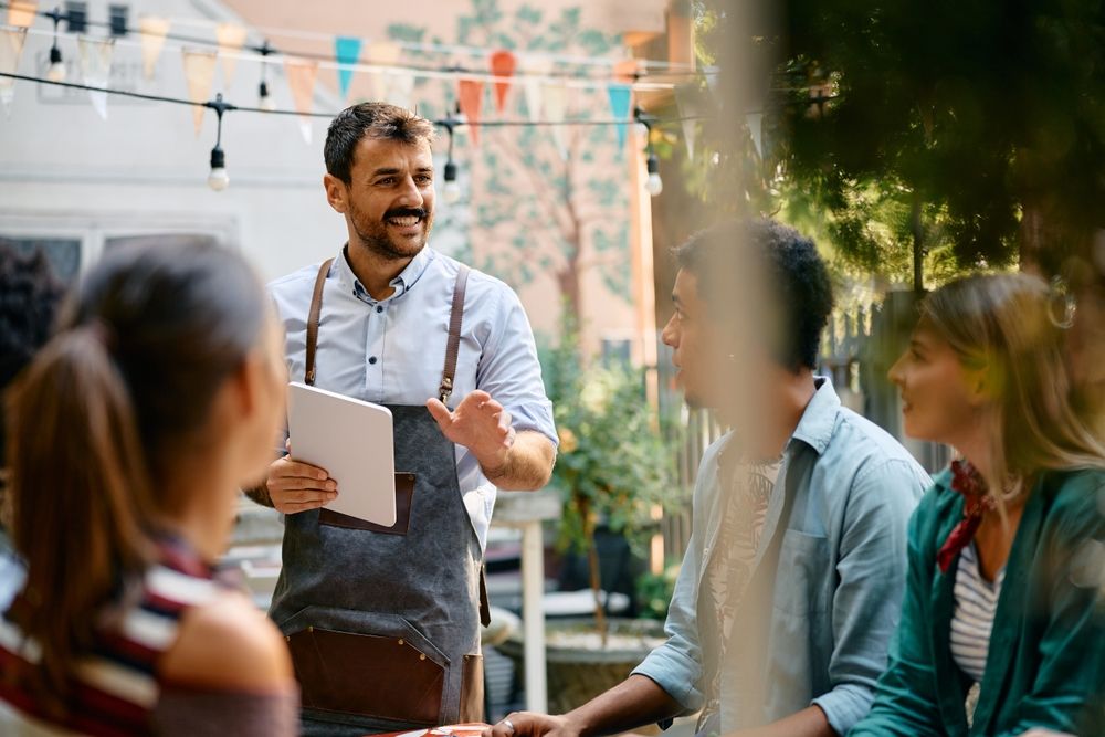 Happy,Waiter,Talking,To,Group,Of,Guests,In,A,Cafe.