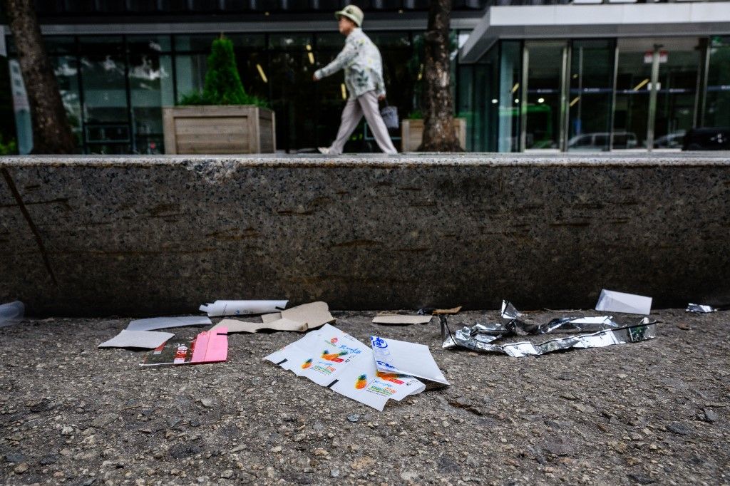 A pedestrian walks along a pavement past pieces of North Korean food packaging, sweet wrappers and paper suspected to be from trash balloons sent from North Korea, in Seoul on July 24, 2024. North Korean sweet wrappers and packets of crackers and other snacks made at a factory once visited by leader Kim Jong Un were found by AFP reporters on Seoul streets on July 24. (Photo by Anthony WALLACE / AFP)