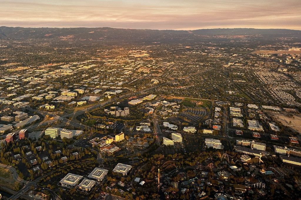 An aerial image taken on July 3, 2024 shows roller coasters at the the Six Flags Entertainment Corp. California's Great America amusement park (R), Mission Valley College (C), along with Silicon Valley area corporate office buildings and homes after sunrise above Santa Clara, California. (Photo by Patrick T. Fallon / AFP)