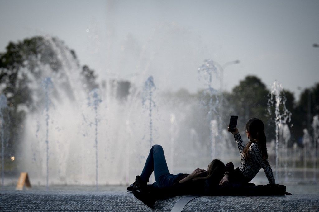 Two women are seen enjoying the weather while using a mobile phone in the fountain park in Warsaw, Poland on 06 June, 2024. (Photo by Jaap Arriens/NurPhoto) (Photo by Jaap Arriens / NurPhoto / NurPhoto via AFP)