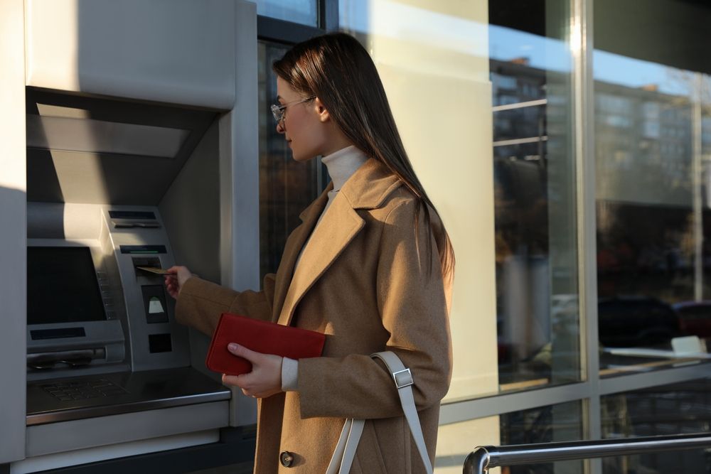 Young,Woman,Using,Cash,Machine,For,Money,Withdrawal,Outdoors