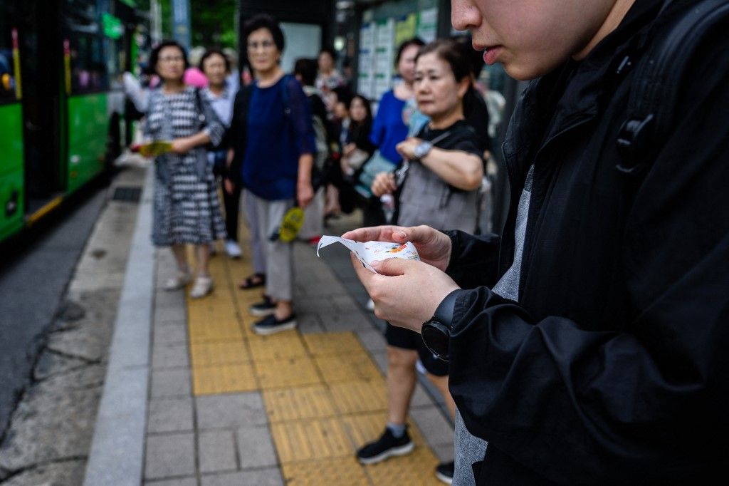 A commuter looks at North Korean confectionary packaging suspected to be from trash balloons sent from North Korea while waiting at a bus stop in Seoul on July 24, 2024. North Korean sweet wrappers and packets of crackers and other snacks made at a factory once visited by leader Kim Jong Un were found by AFP reporters on Seoul streets on July 24. (Photo by Anthony WALLACE / AFP)