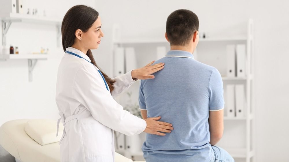 Female,Doctor,Checking,Posture,Of,Young,Man,In,Clinic