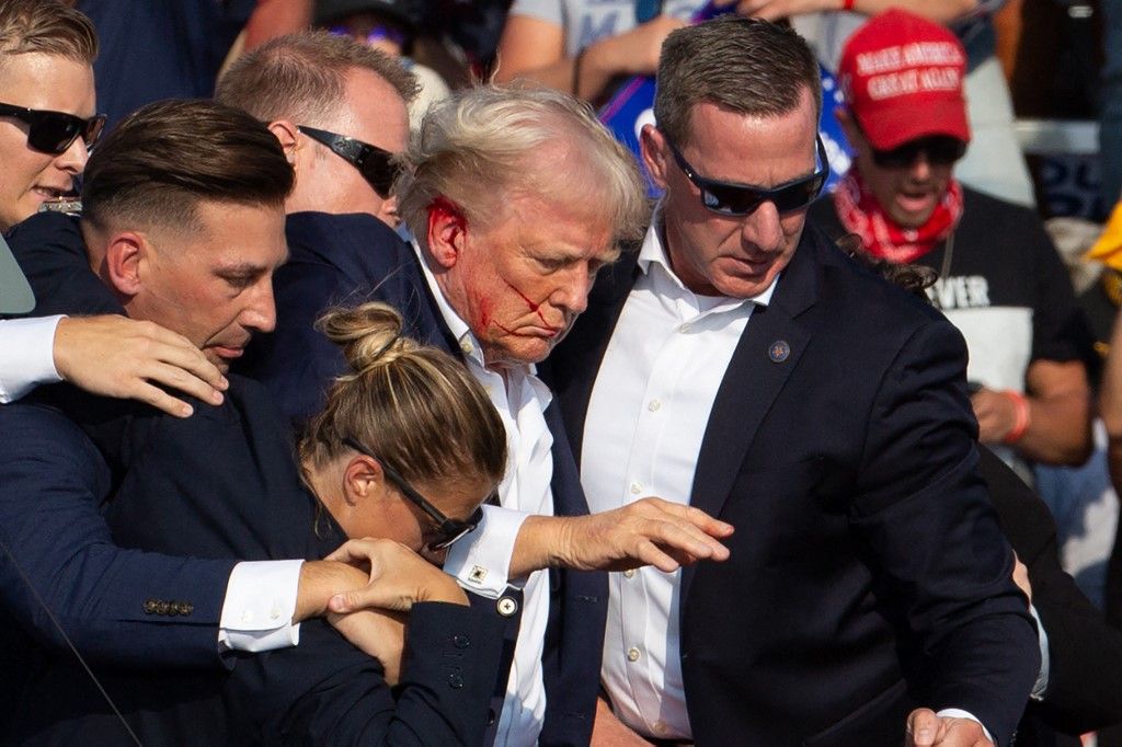 US Republican candidate Donald Trump is seen with blood on his face surrounded by secret service agents as he is taken off the stage at a campaign event at Butler Farm Show Inc. in Butler, Pennsylvania, on July 13, 2024. Trump was hit in the ear in an apparent assassination attempt by a gunman at a campaign rally on Saturday, in a chaotic and shocking incident that will fuel fears of instability ahead of the 2024 US presidential election. The 78-year-old former president was rushed off stage with blood smeared across his face after the shooting in Butler, Pennsylvania, while the gunman and a bystander were killed and two spectators critically injured. (Photo by Rebecca DROKE / AFP) / QUALITY REPEAT