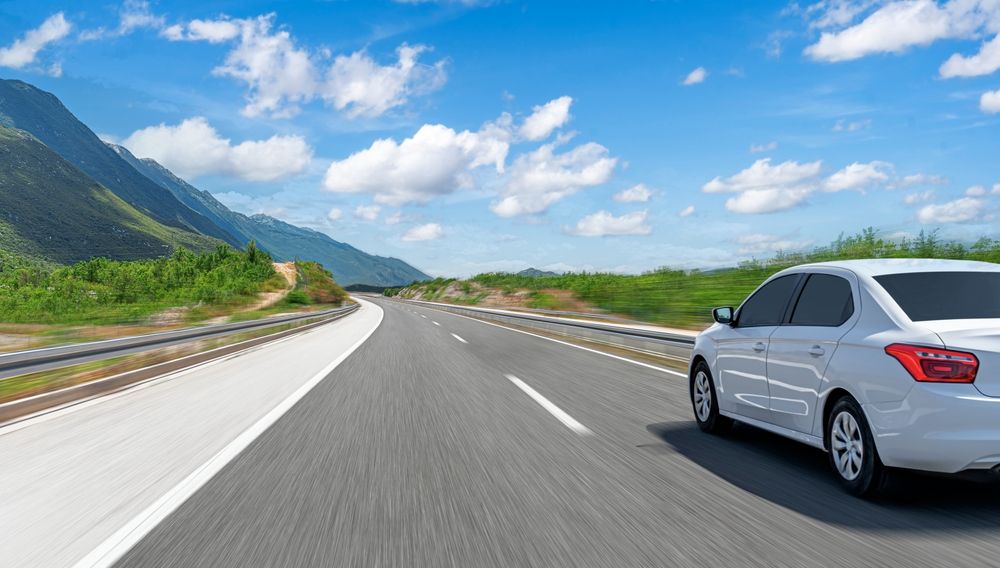 A,White,Car,Drives,Along,The,Highway,Against,The,Backdrop