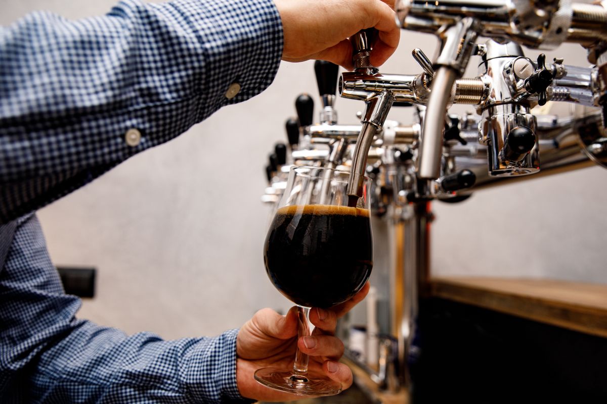 The bartender pours fresh dark beer from tap in the pub.