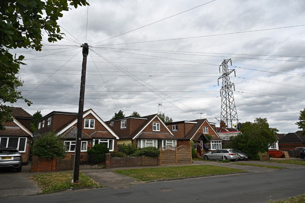 Az Ofgem az ukrajnai háború miatt is növeli a brit háztartások rezsijét.A photograph taken on August 21, 2024 shows electricity pylons next to houses in West Byfleet, Surrey, south of London. Britain's Energy regulator Ofgem will on August 23, 2024 announce the latest quarterly energy price cap, for October to December. (Photo by Justin TALLIS / AFP)