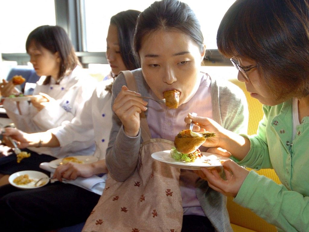 South Korean students eat Camembert and Kimchi (Camembert et Kimchi en beignet) at a French-Korean food exhibition at Le Cordon Bleu Korea in Seoul, 19 October 2004.  The event is part of South Korean government's campaign to promote Kimchi, a traditional Korean dish of fermented cabbage. AFP PHOTO/KIM JAE-HWAN (Photo by KIM JAE-HWAN / AFP)