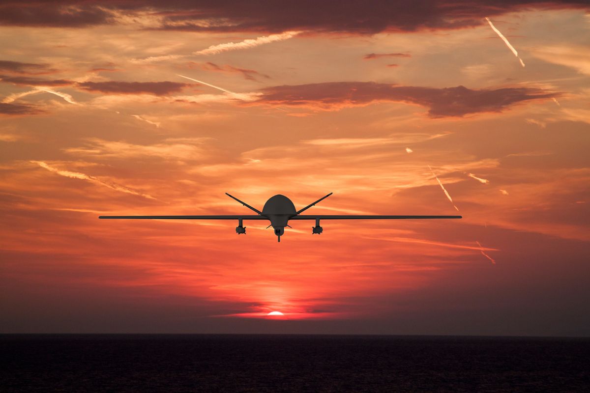 Silhouette of spy drone flying over the sea (UAV) and on background beautiful view of sun hiding behind sea surface.  sunset sky is orange with clouds and condensation traces, drón