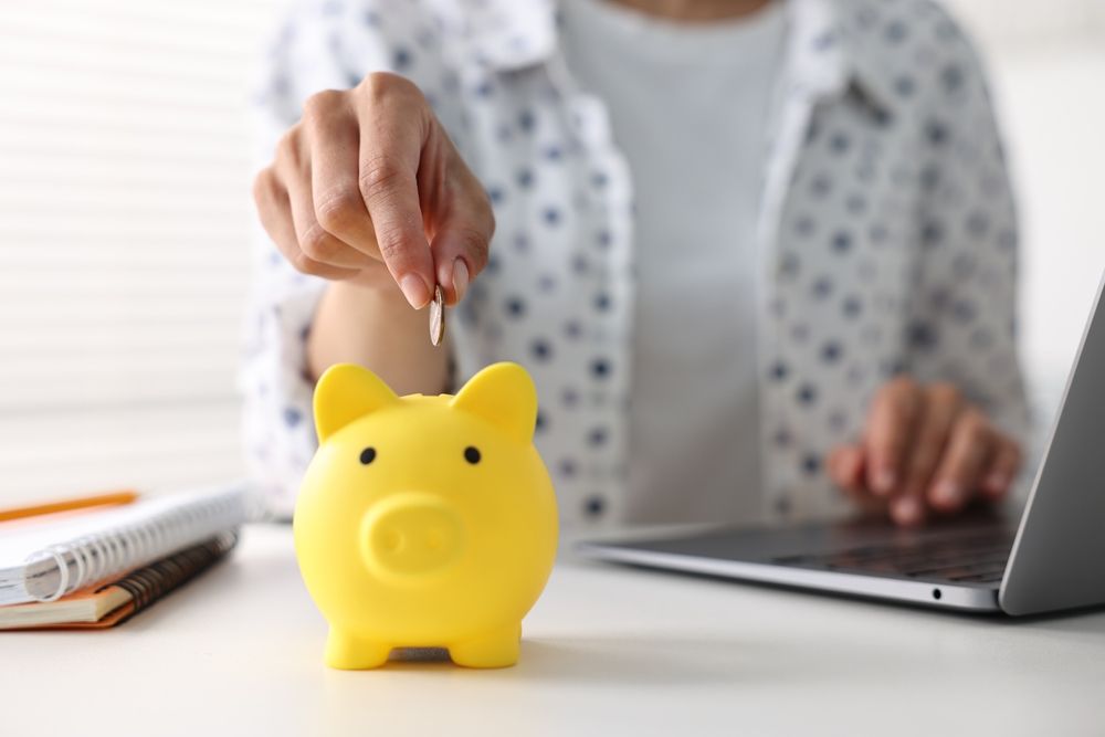 Woman,Putting,Coin,Into,Piggy,Bank,At,White,Table,Indoors,