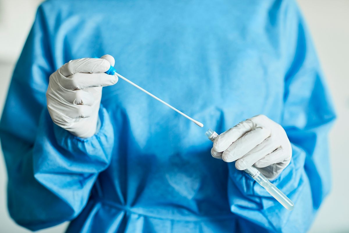 Midsection of female doctor with swab test sample during COVID-19 crisis. Female medical professional is holding test tube in hospital. She is wearing protective suit.