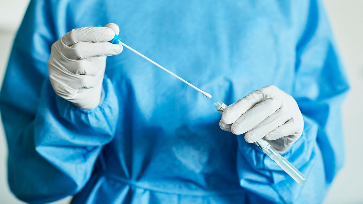 Midsection of female doctor with swab test sample during COVID-19 crisis. Female medical professional is holding test tube in hospital. She is wearing protective suit. szlovák