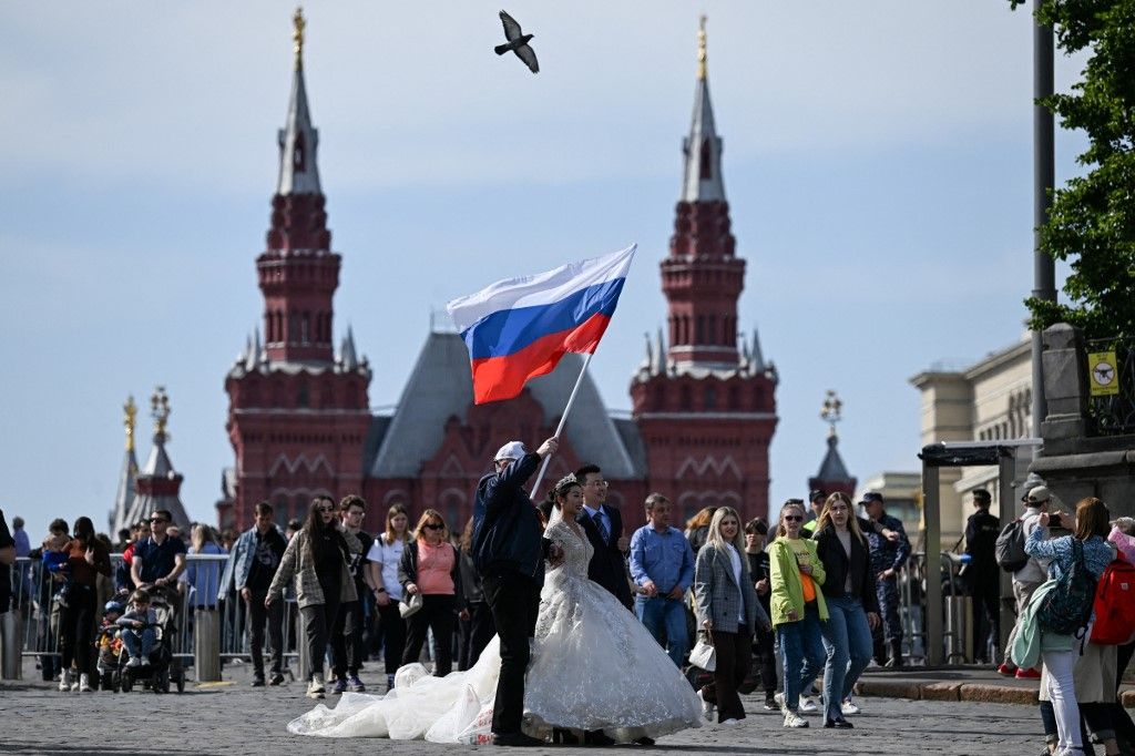 A man waves Russian national flag next to a couple in wedding attire after the patriotic concert at the Red square in downtown Moscow ahead the Russia Day on June 11, 2023. (Photo by Kirill KUDRYAVTSEV / AFP)