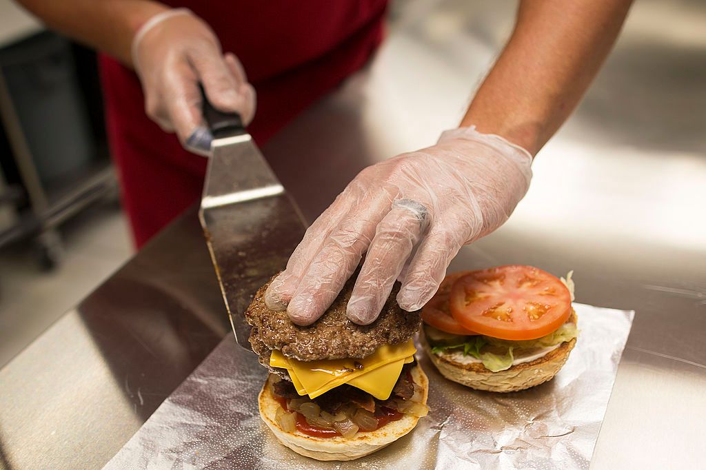 An employee places a beef pattie onto a hamburger bun in the kitchen kikötői sztrájk