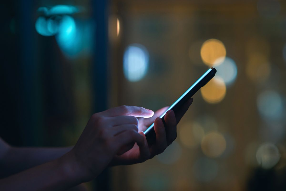 Close up of woman's hand using smartphone in the dark, against illuminated city light bokeh