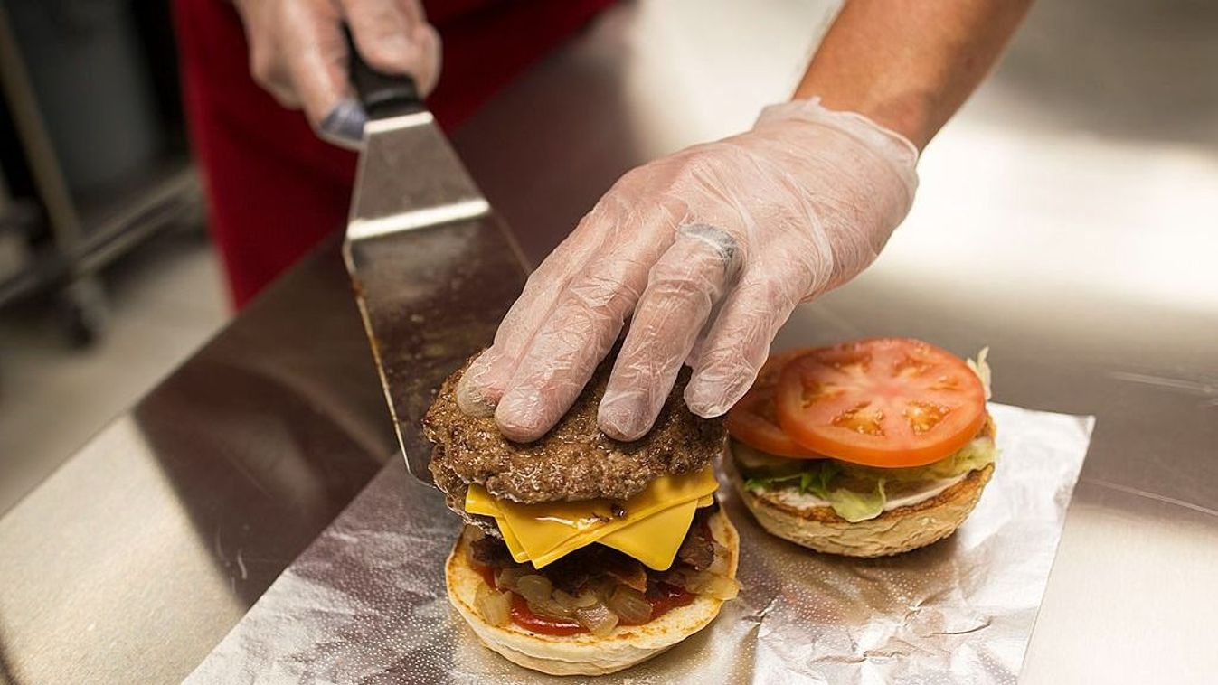 An employee places a beef pattie onto a hamburger bun in the kitchen kikötői sztrájk