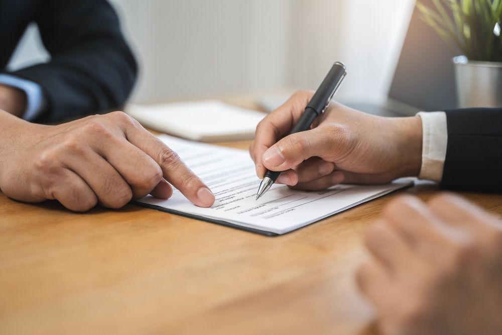 Businessman,Sitting,At,Desk,Holds,Pen,Signing,Contract,Paper,,Lease