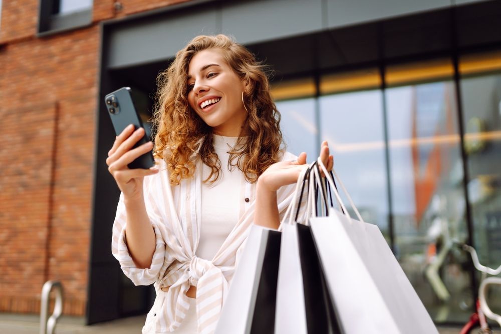 Young,Woman,Use,Of,Mobile,Phone,And,Hold,With,Shopping vásárlás