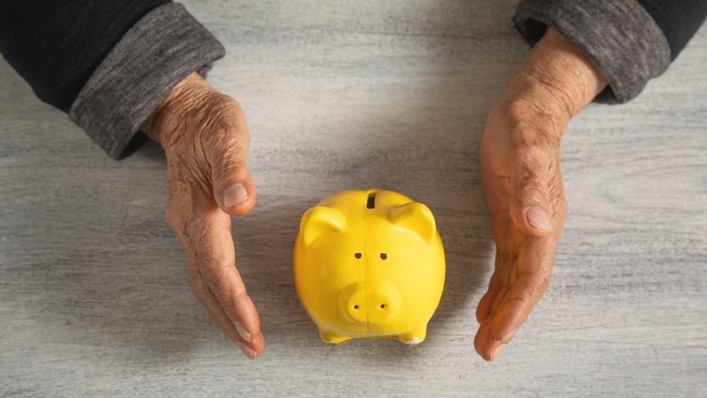 Elderly,Woman,Holding,A,Piggy,Bank,On,The,Table.