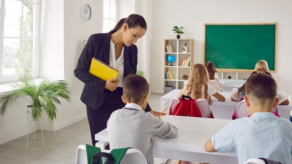 Female,Teacher,Holding,Yellow,Folder,Helps,Caucasian,Schoolkids,To,Finish amerikai oktatás