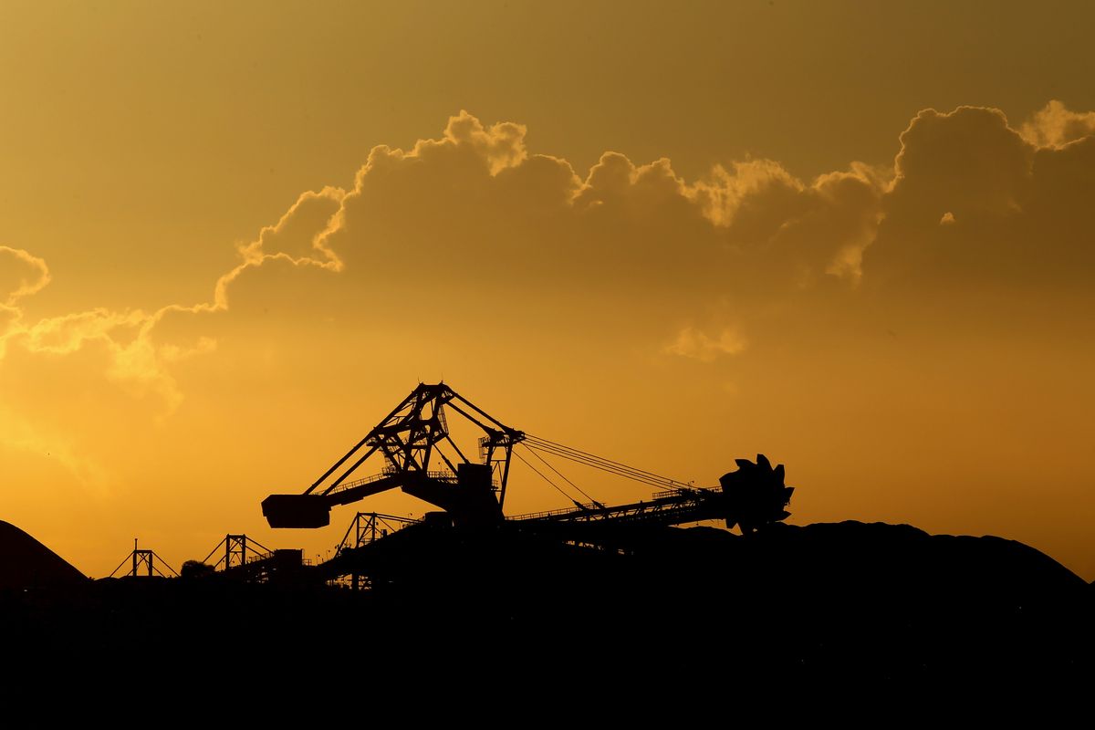 A stacker-reclaimer operates next to stockpiles of coal. glencore