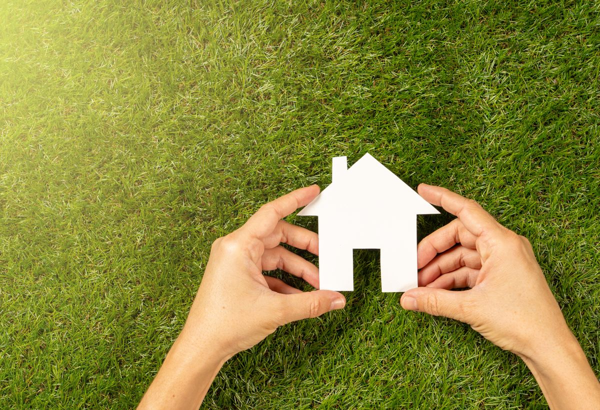 Conceptual,Picture,Of,Woman,Hands,Holding,White,House,Over,Green