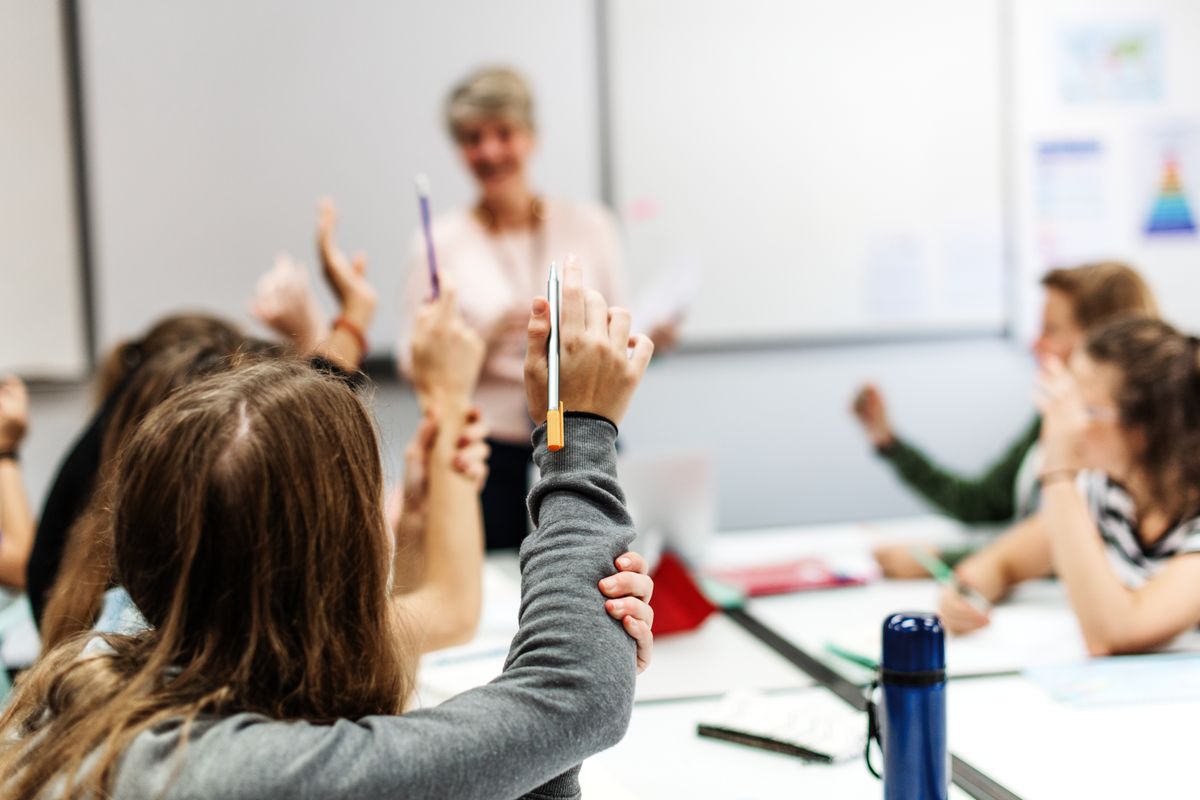 pedagógus Students,Raising,Hands,In,A,Classroom.,Female,Teacher,Engaging,With