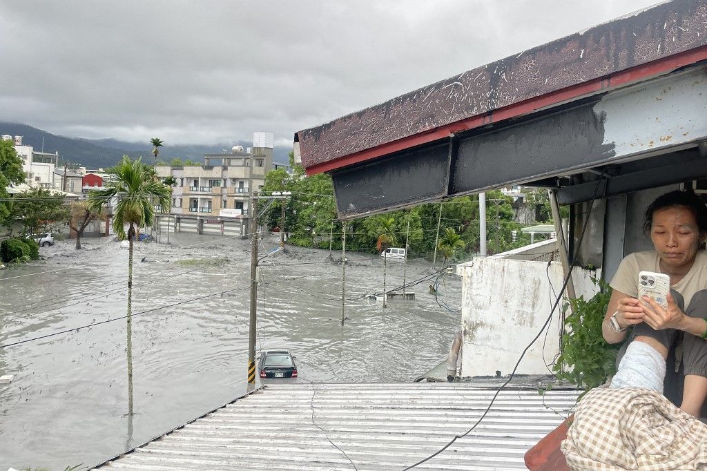 A resident uses her mobile phone while sitting on the roof of a house, as water from a burst landslide dam overflows and floods the area in Hualien on September 23, 2025, as a result of heavy rain due to Super Typhoon Ragasa. The super typhoon was generat