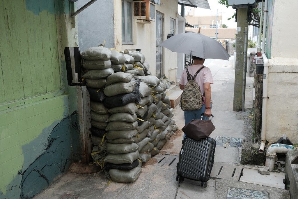 Stacked sandbags are seen in an alley as a woman with luggage walks past in the low-lying coastal village of Lei Yue Mun in preparation for Super Typhoon Ragasa in Hong Kong on September 23, 2025. Hong Kong shut schools and cancelled flights on September 