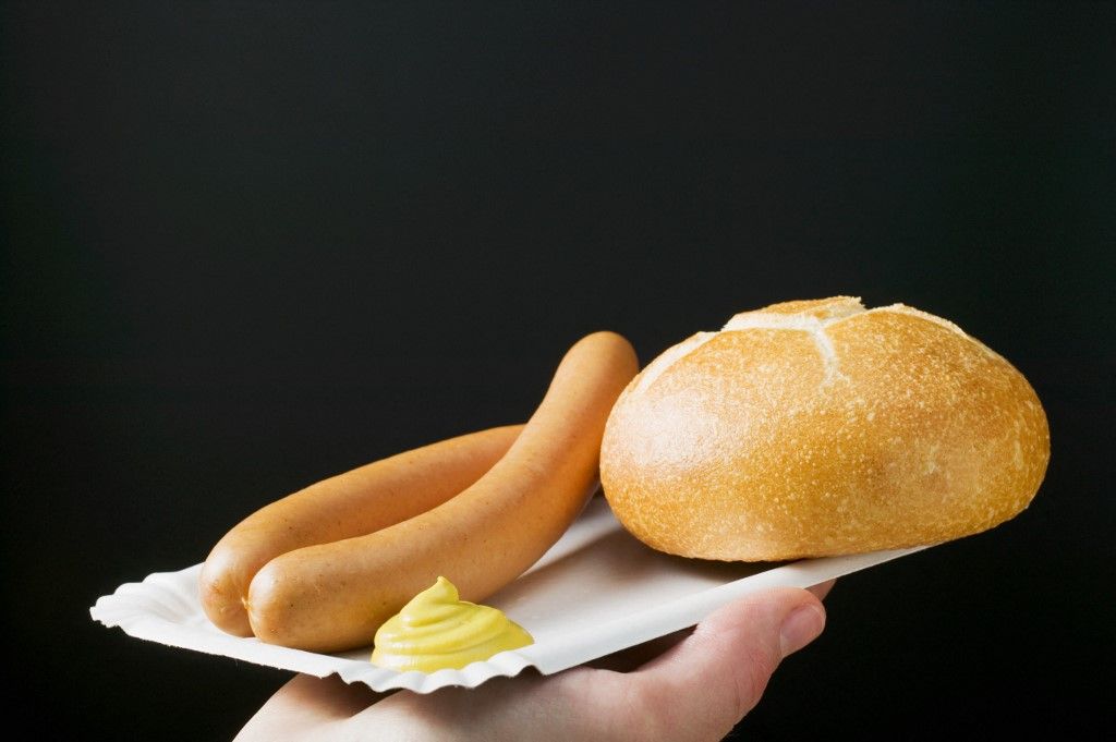 Hand holding frankfurters, roll & mustard on paper plate virsli szilveszter