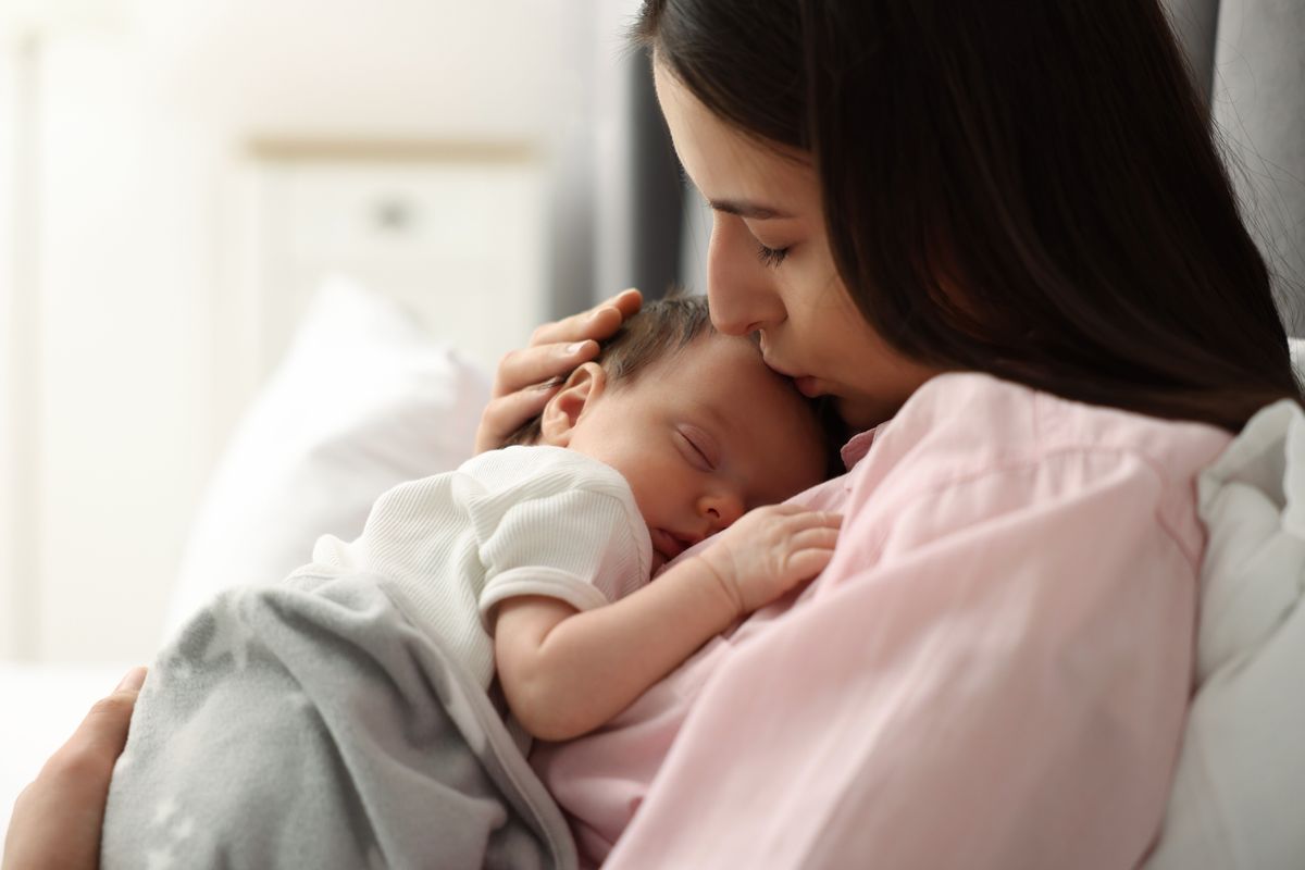 Mother,Kissing,Her,Sleeping,Newborn,Baby,In,Bed,At,Home