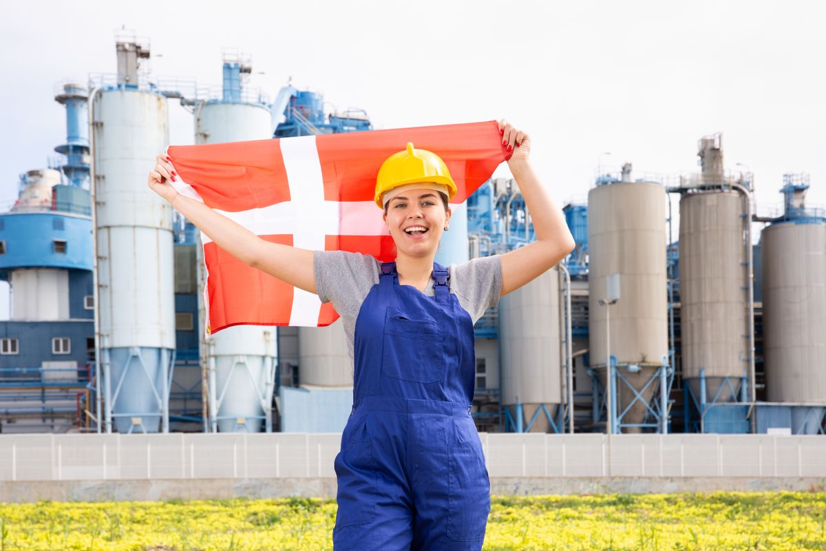 Cheerful,Female,Worker,In,Hardhat,With,Danish,Flag,Standing,In