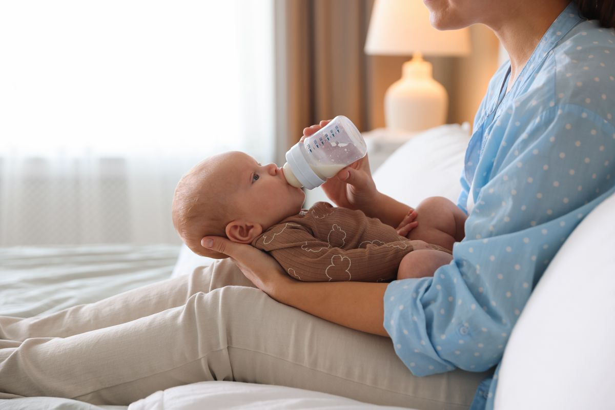 tápszer Mother,Feeding,Her,Little,Baby,With,Bottle,On,Bed,,Closeup