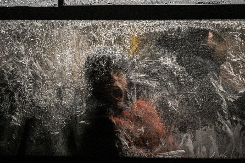 A youth tries to remove frost from a frozen window as he rides a bus during a winter evening in Kyiv on January 15, 2026, amid the Russian invasion of Ukraine. (Photo by Sergei GAPON / AFP)