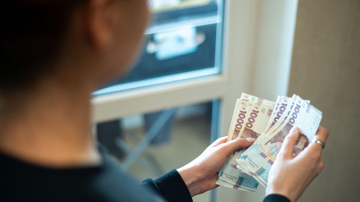 Women,Holds,Various,Banknotes,While,Standing,In,A,Bright,Room ukrán hrivnya ukrajna
