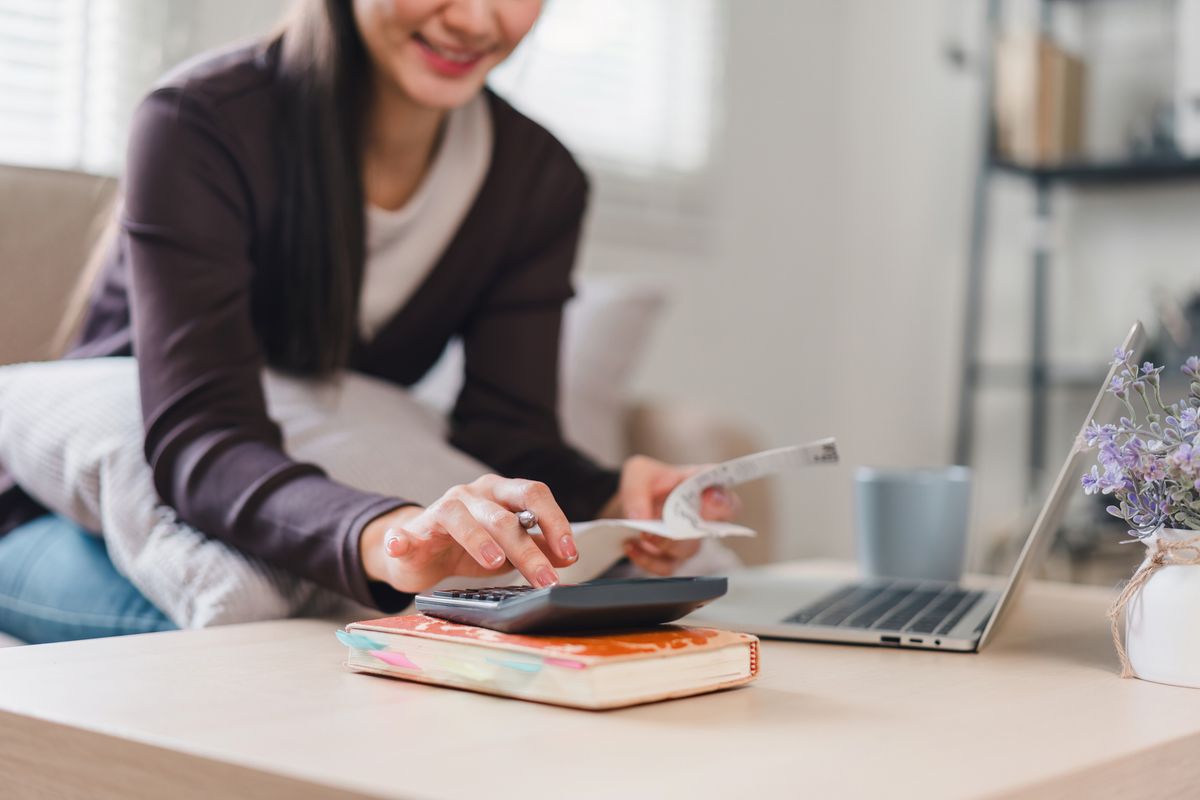 Close up of woman using calculator and holding receipts while managing finances at home.
