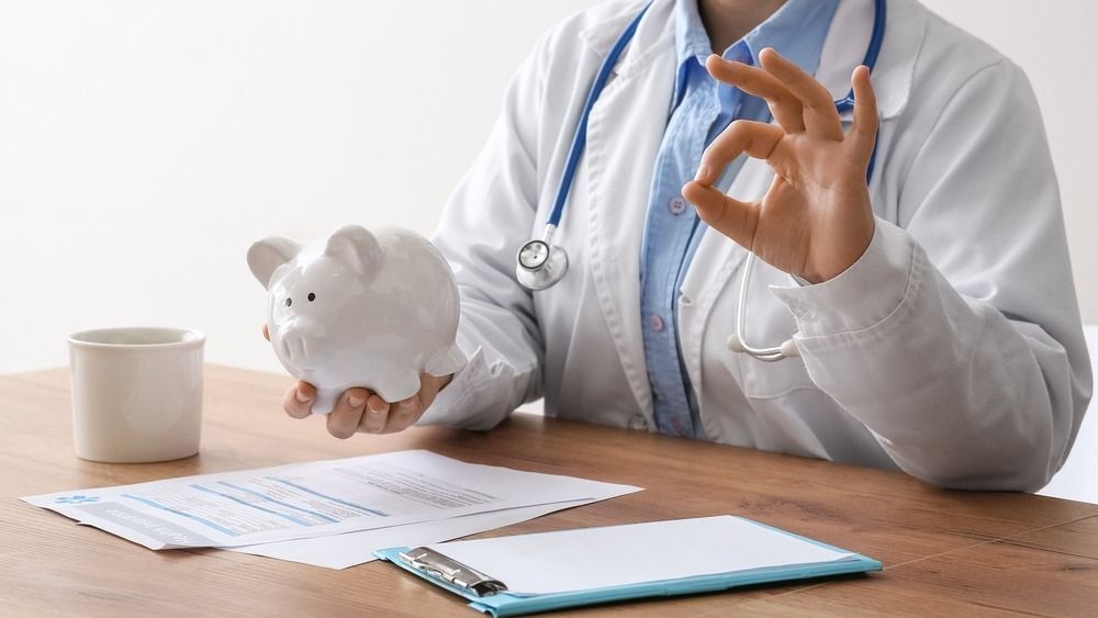egészségpénztár,Female,Doctor,Holding,Piggy,Bank,And,Showing,Ok,Gesture,At